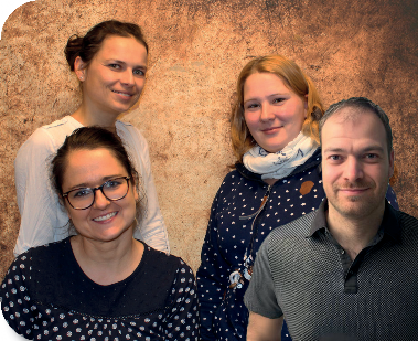 Vier lächelnde Vorstandsmitglieder des Fördervereins stehen gemeinsam vor einer hellen Wand im Kindergarten. Sie tragen legere Kleidung und vermitteln eine freundliche, einladende Atmosphäre